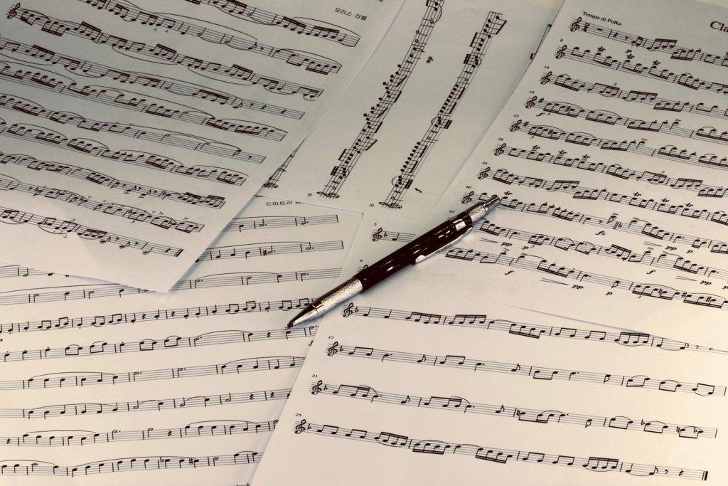 A pen sits on top of scattered pages of sheet music.